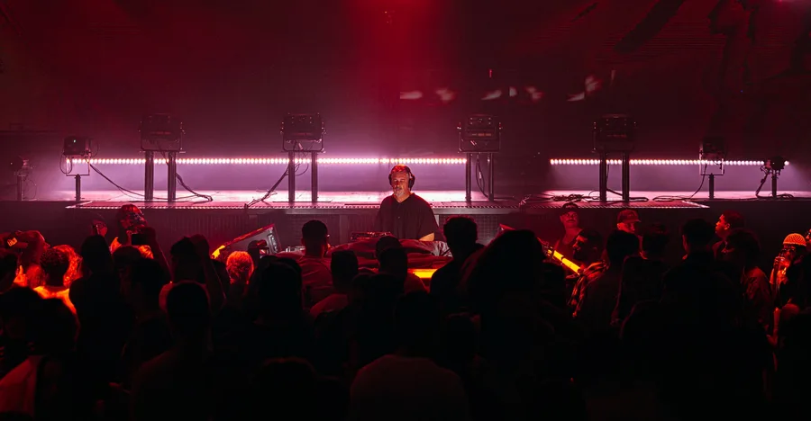 DJ INO behind the decks in front of a red lit crowd